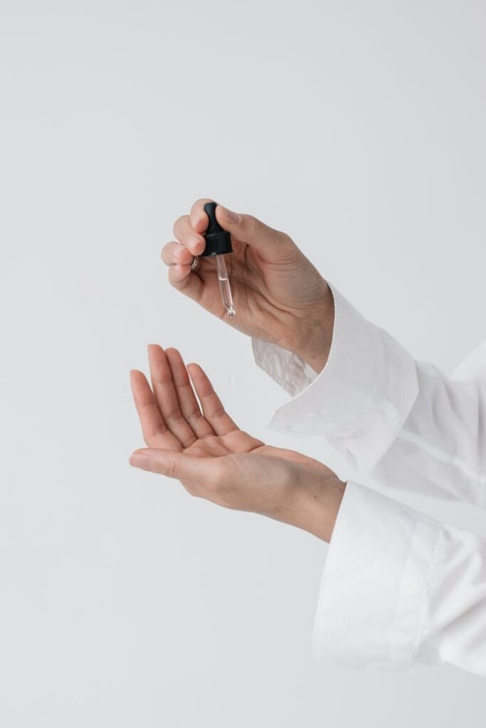 A person's hands applying skincare serum using a dropper for a beauty routine.